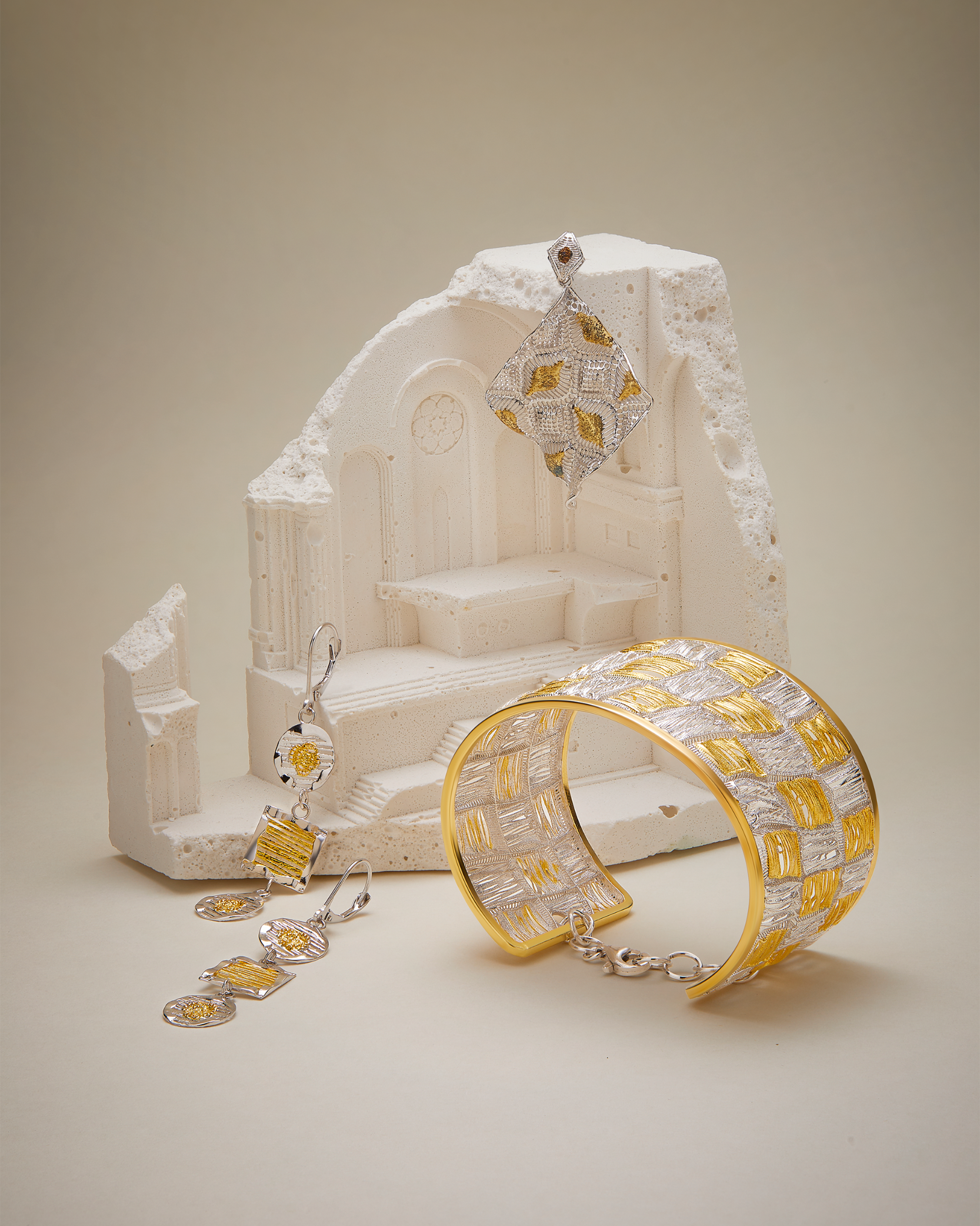 Gold and silver jewelry set with a white architectural model on a beige background