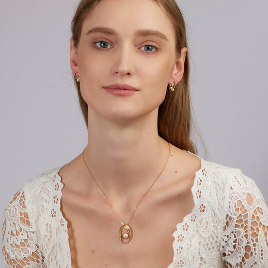 Woman wearing a gold necklace with an oval pendant against a plain background