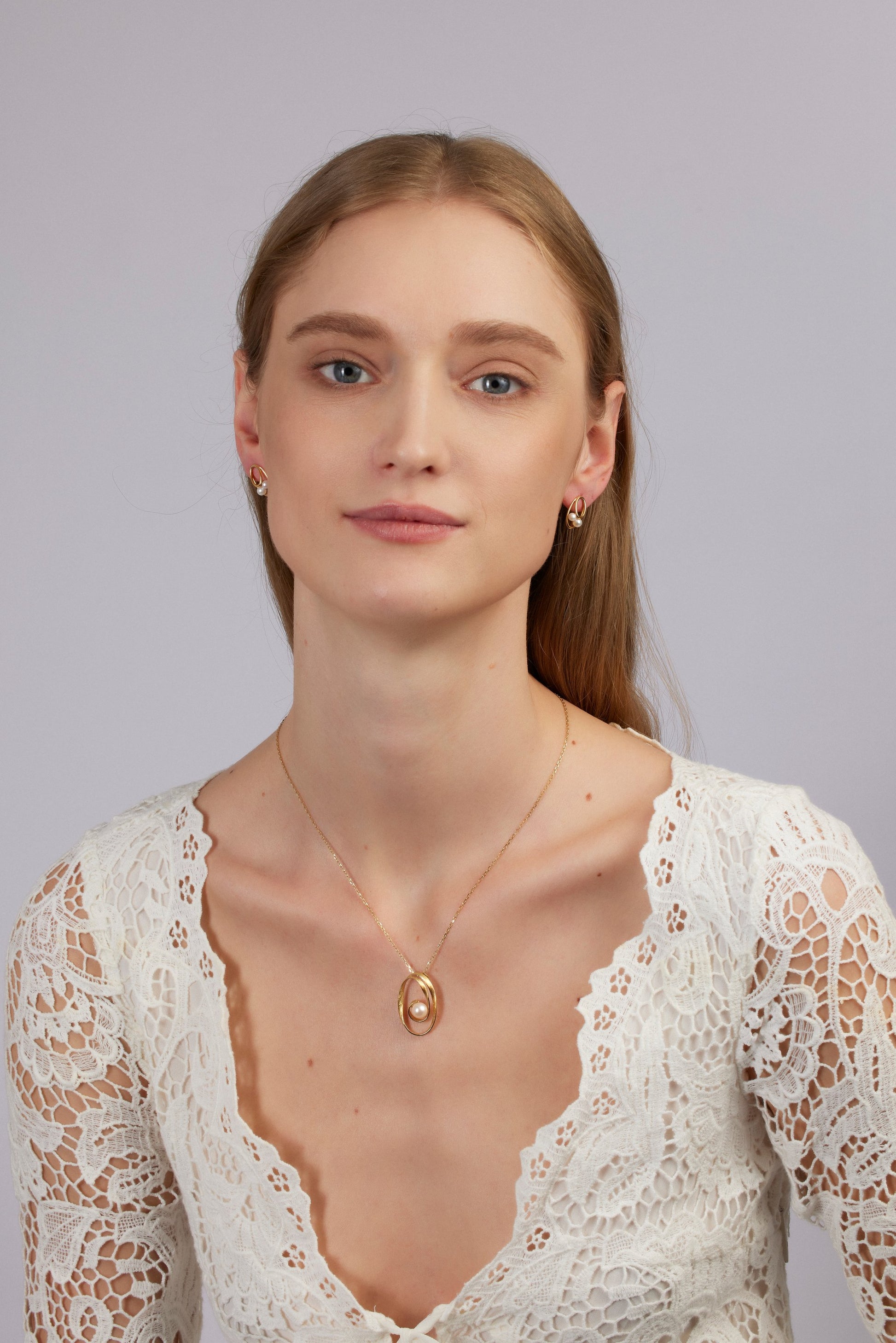 Woman wearing a gold necklace with an oval pendant against a plain background