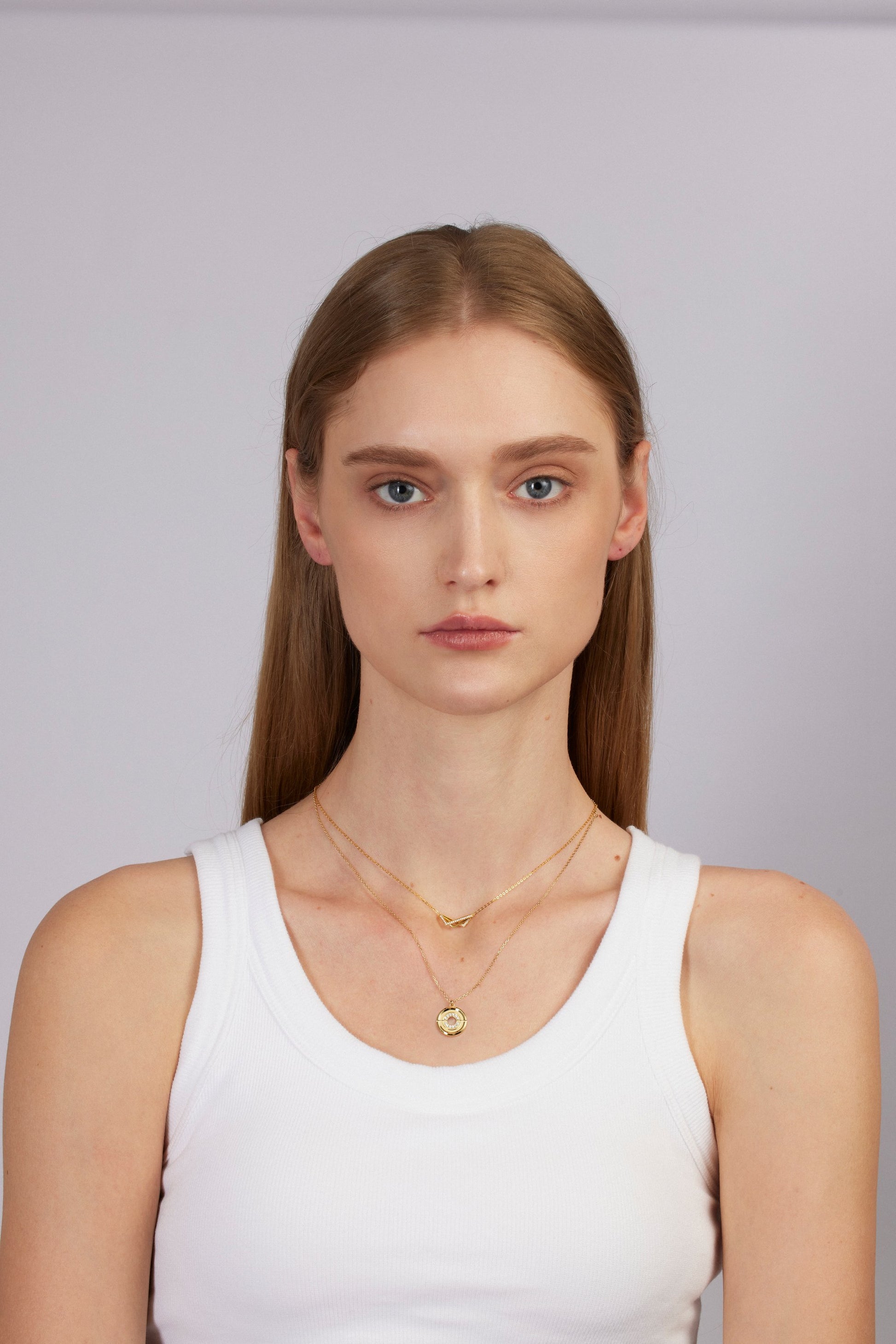 Woman wearing a white tank top and gold necklace against a plain background