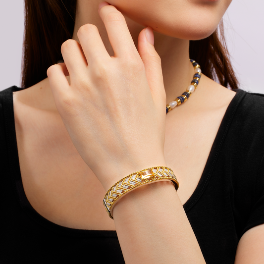 Woman wearing a gold bracelet and necklace on a plain background