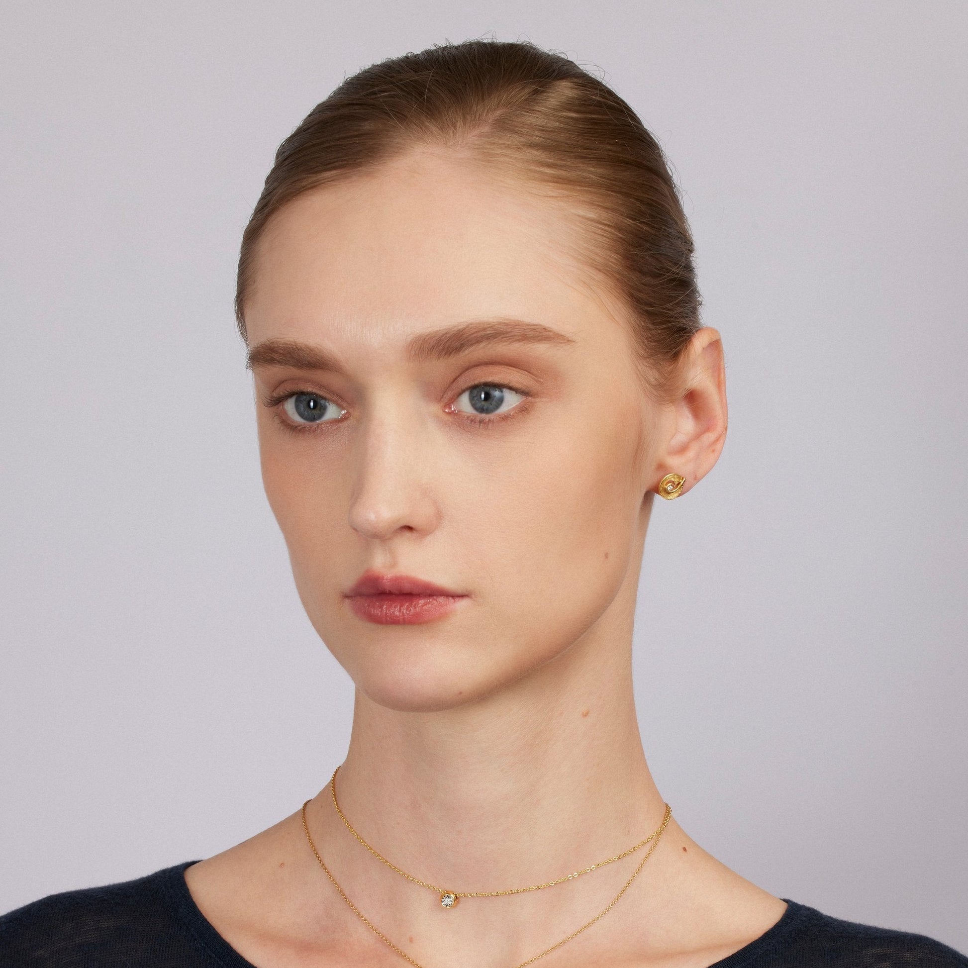 Woman wearing gold necklaces against a plain background