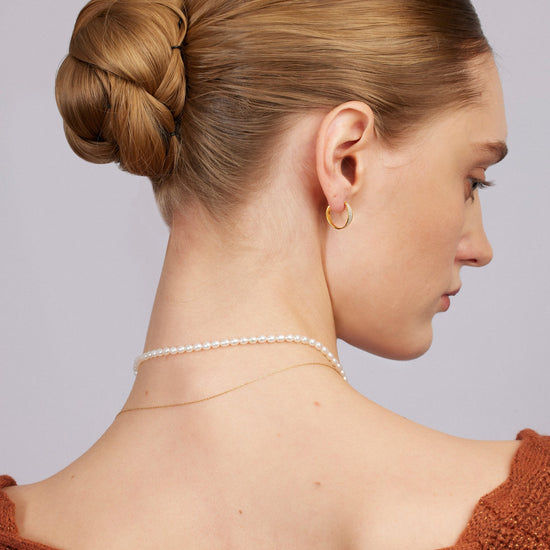 Woman with styled hair and jewelry against a neutral background