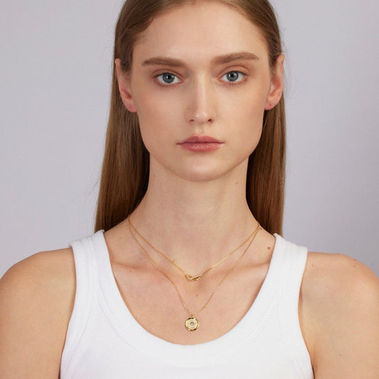 Woman wearing a white tank top and gold necklace against a plain background