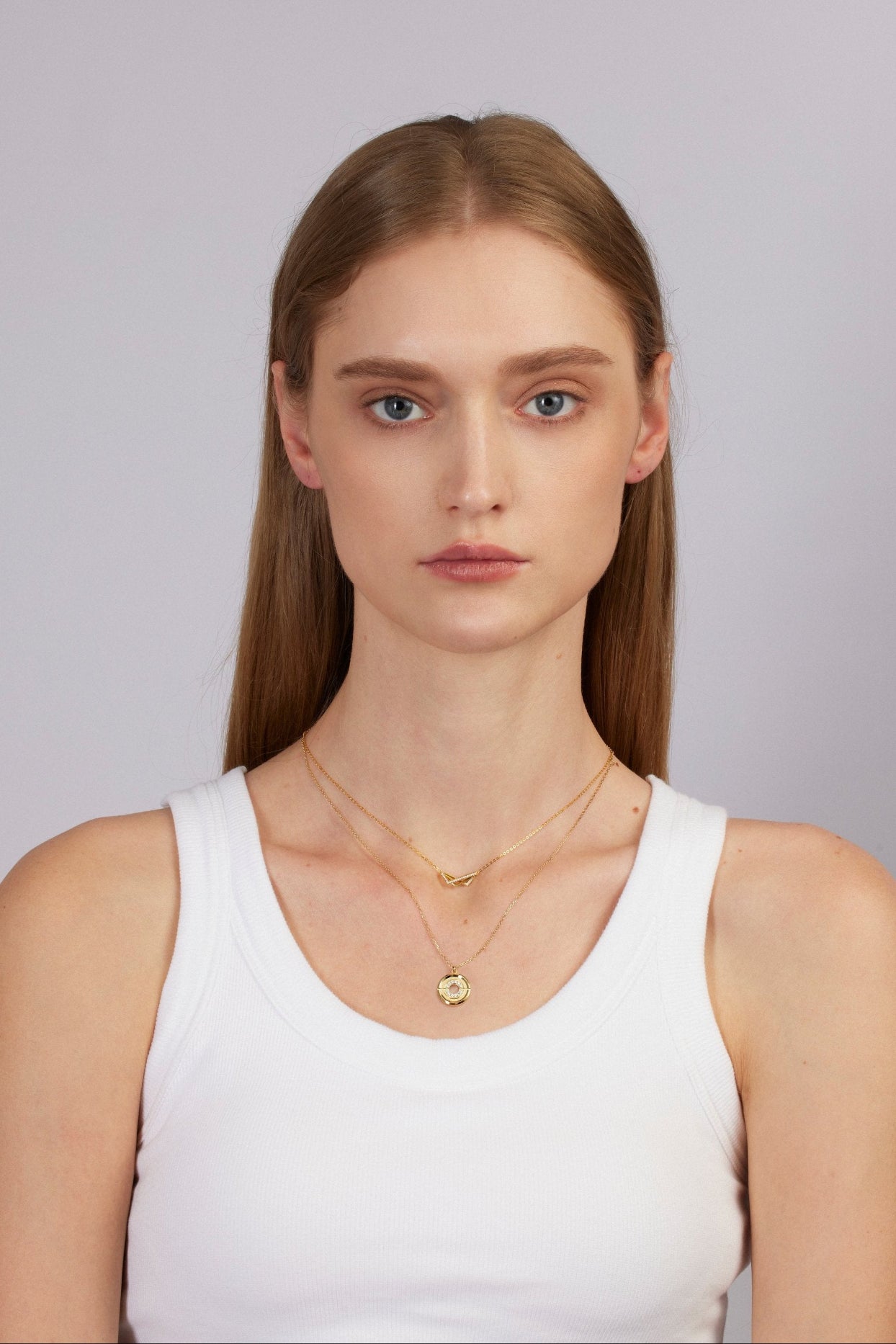Woman wearing a white tank top and gold necklace against a plain background