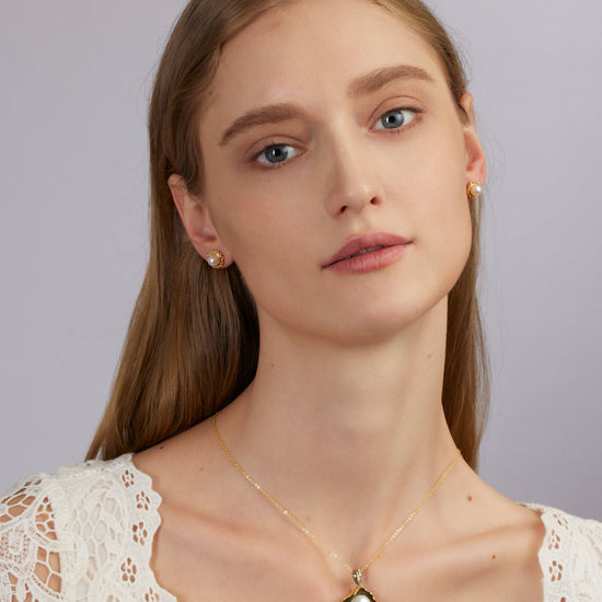 Woman wearing a gold necklace with a pearl pendant against a gray background