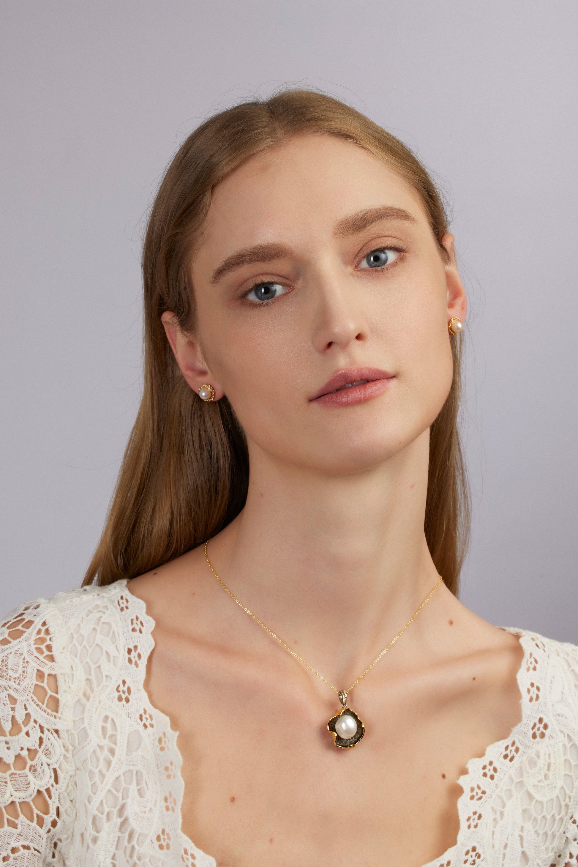 Woman wearing a gold necklace with a pearl pendant against a gray background