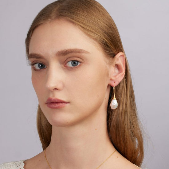 Woman wearing a pearl earring and gold necklace against a plain background