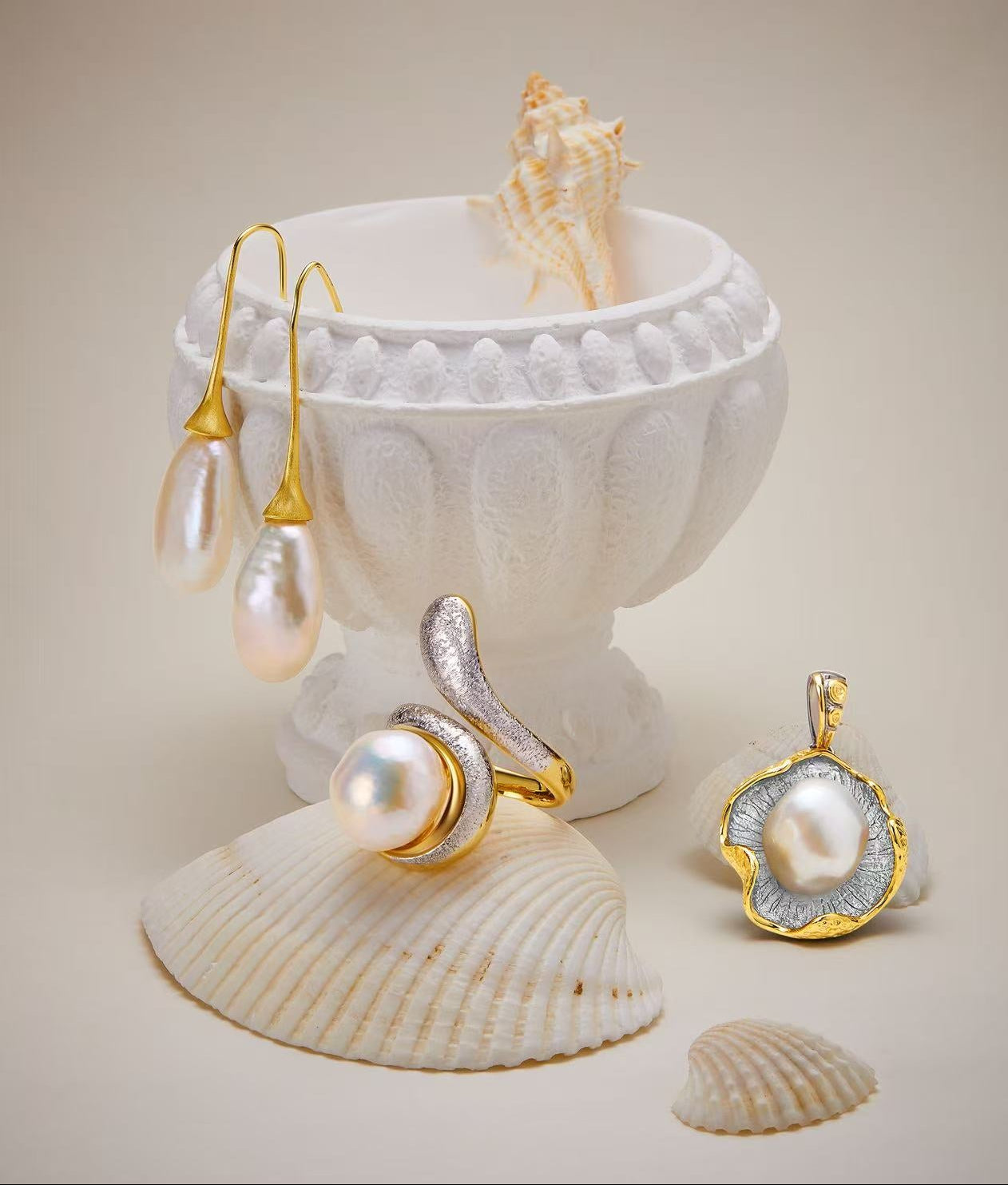 Pearl jewelry set including earrings and a pendant displayed on a shell with a beige background.