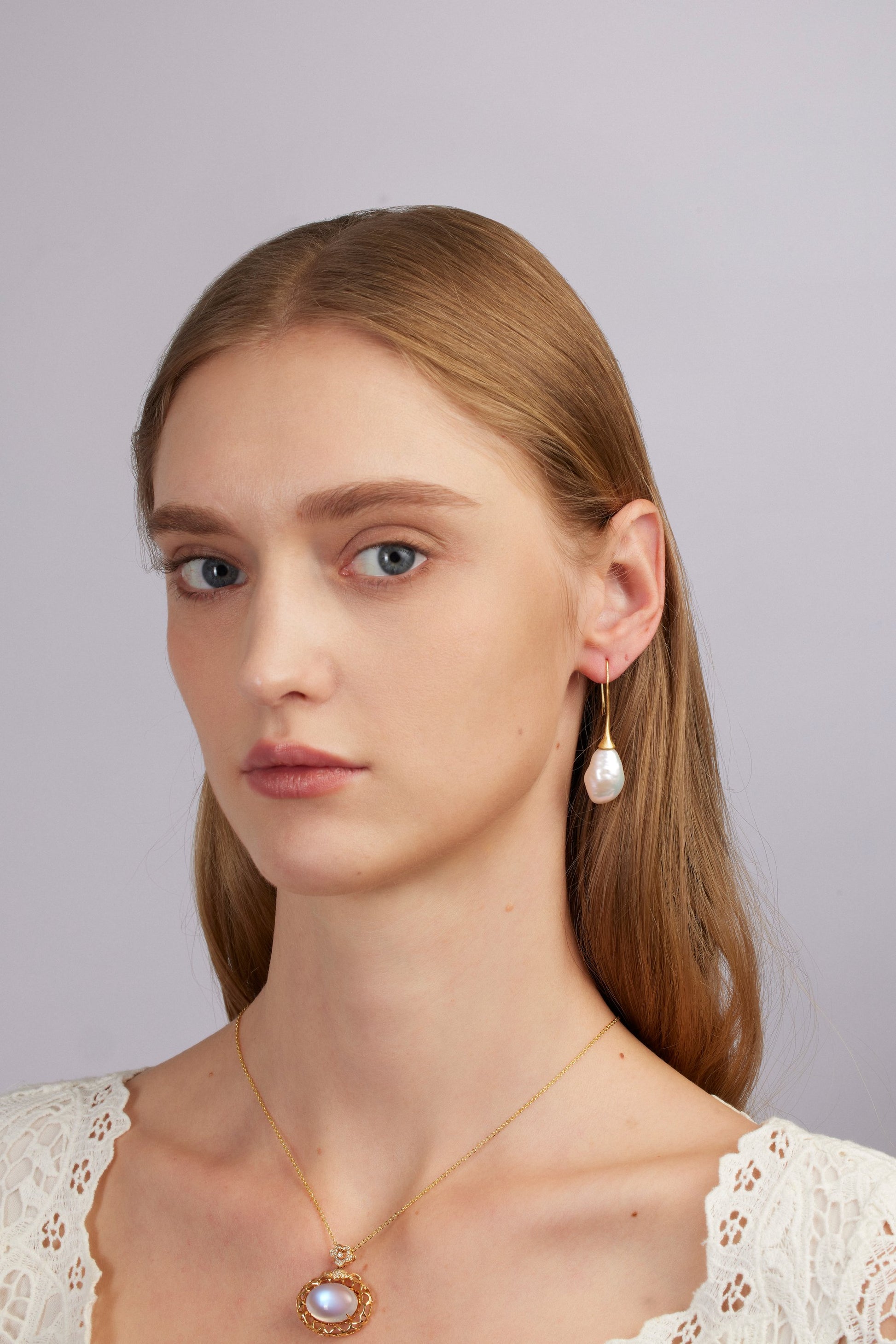 Woman wearing pearl earrings and a necklace against a plain background