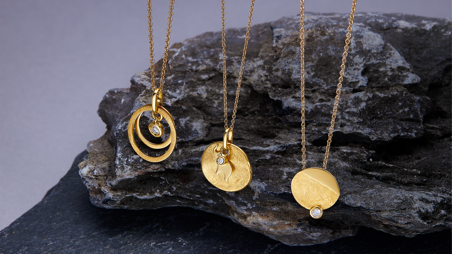 Three gold necklaces with circular pendants on a dark surface
