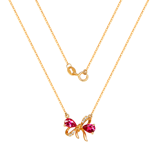 Gold necklace with a red gemstone bow pendant on a white background
