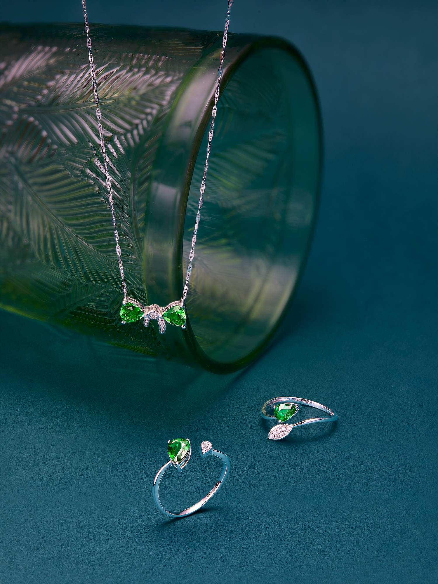 18k white gold jewelry set with green gemstones on a teal background