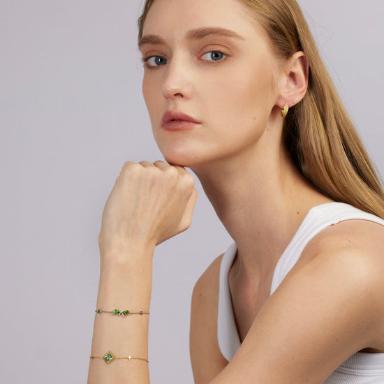 Woman wearing a white tank top and gold jewelry against a light gray background