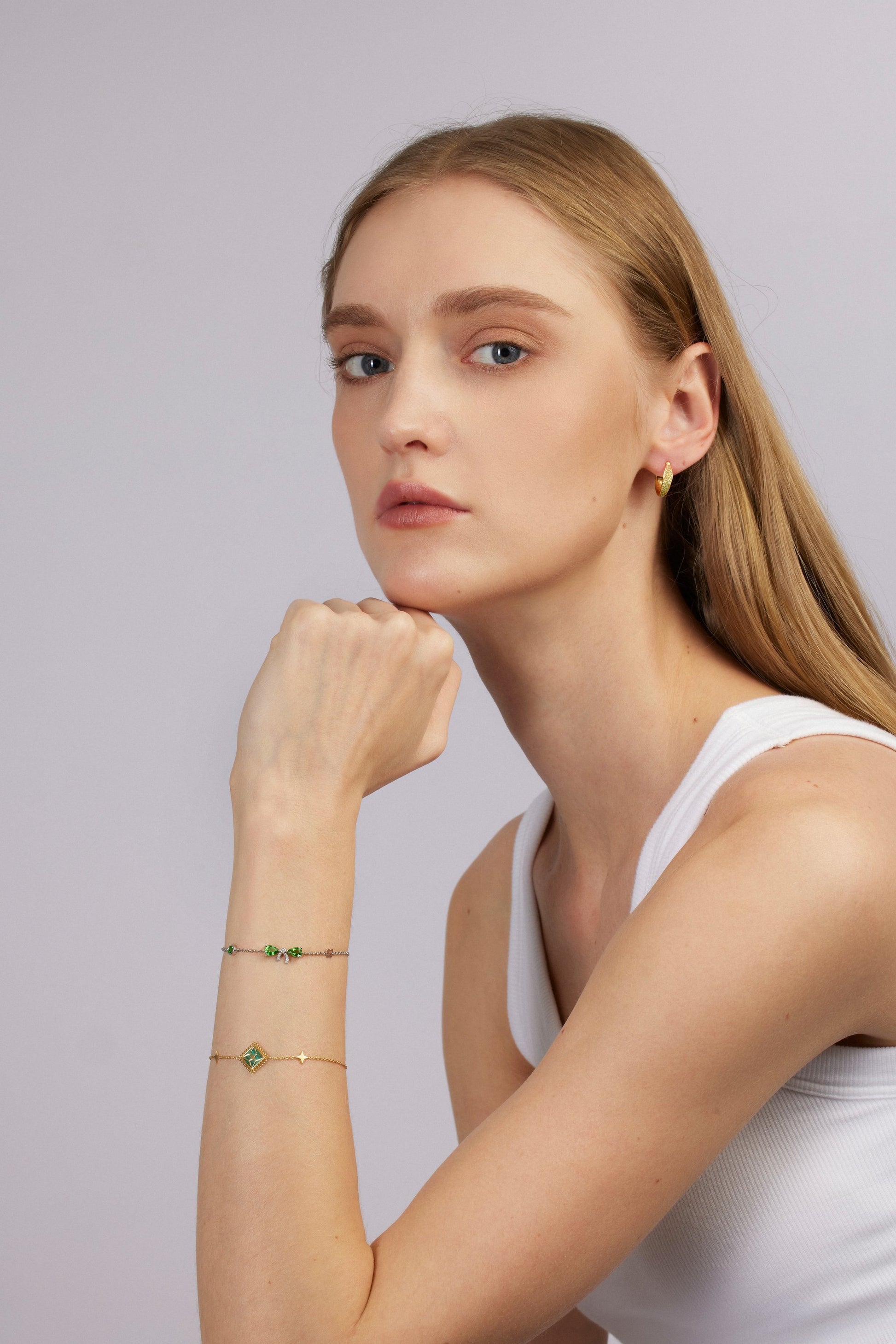 Woman wearing a white tank top and gold jewelry against a light gray background